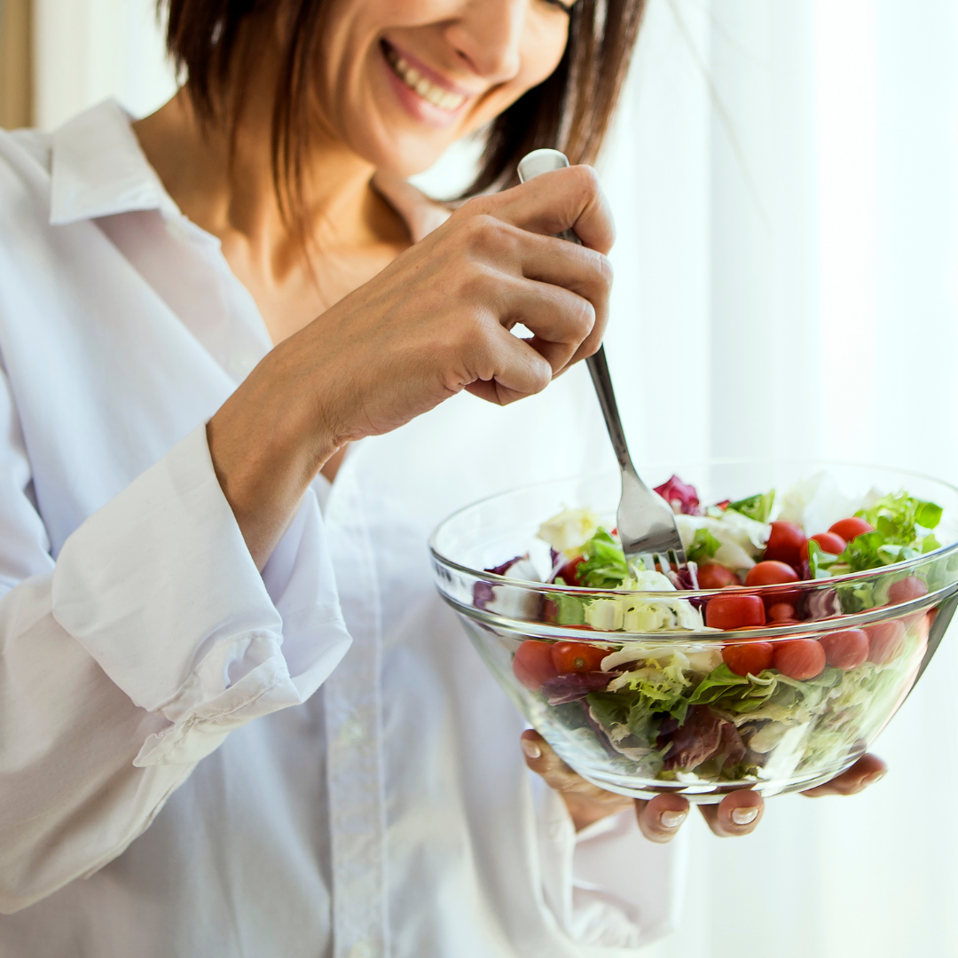 woman eating healthy meal from a clear bowl and smiling
